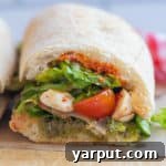 Close-up of a perfectly sliced Caprese salad sandwich, revealing layers of fresh mozzarella, tomatoes, basil, and greens on a toasted baguette