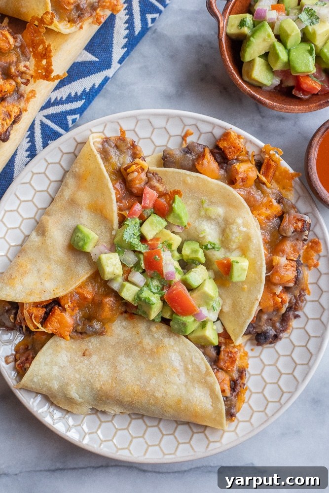 A plate brimming with multiple crispy baked tacos, featuring a delicious sweet potato and black bean filling, garnished with fresh herbs.