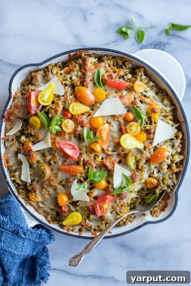 A casserole dish filled with baked pesto orzo pasta, dotted with vibrant cherry tomatoes.