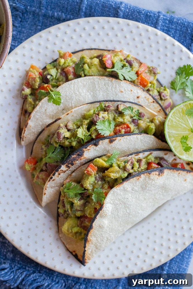 Ultimate Guacamole Tacos 5 Three beautifully presented vegetarian guacamole tacos on a white serving plate, garnished with a fresh lime wedge.
