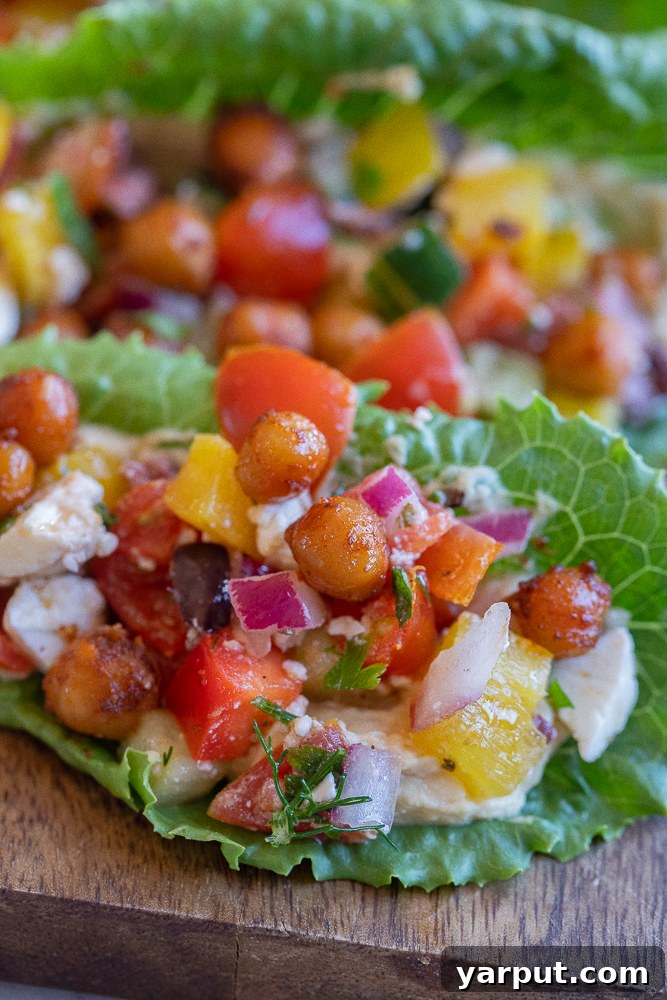 Vibrant Greek Hummus Lettuce Wraps 6 A close-up of a single Greek salad lettuce wrap, highlighting the golden, crispy chickpeas nestled on top of the vibrant vegetable and hummus filling, emphasizing the delightful crunch and texture.