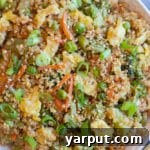 A close-up of a serving of Quinoa Fried Rice in a small bowl, garnished with green onions.