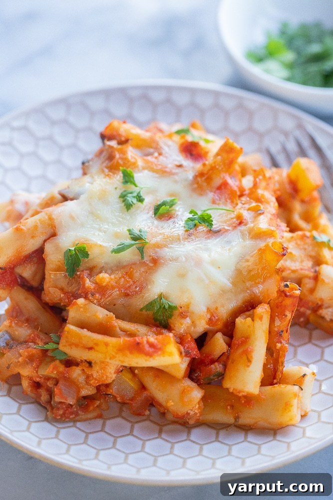 A close-up of a plate of Vegetarian Baked Ziti, showcasing the rich tomato sauce, melted cheese, and visible vegetables, garnished with fresh parsley.