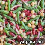 A smaller, focused image of the three-bean salad with basil vinaigrette, ideal for a recipe card thumbnail. It shows a vibrant mix of green beans, kidney beans, and garbanzo beans coated in the dressing, with fresh basil visible.