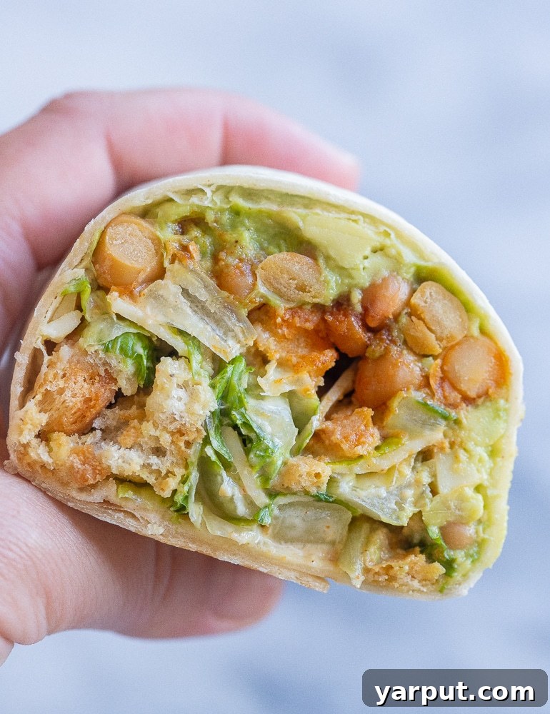 close up of a hand holding a vegetarian chicken Caesar salad wrap that has been cut in half