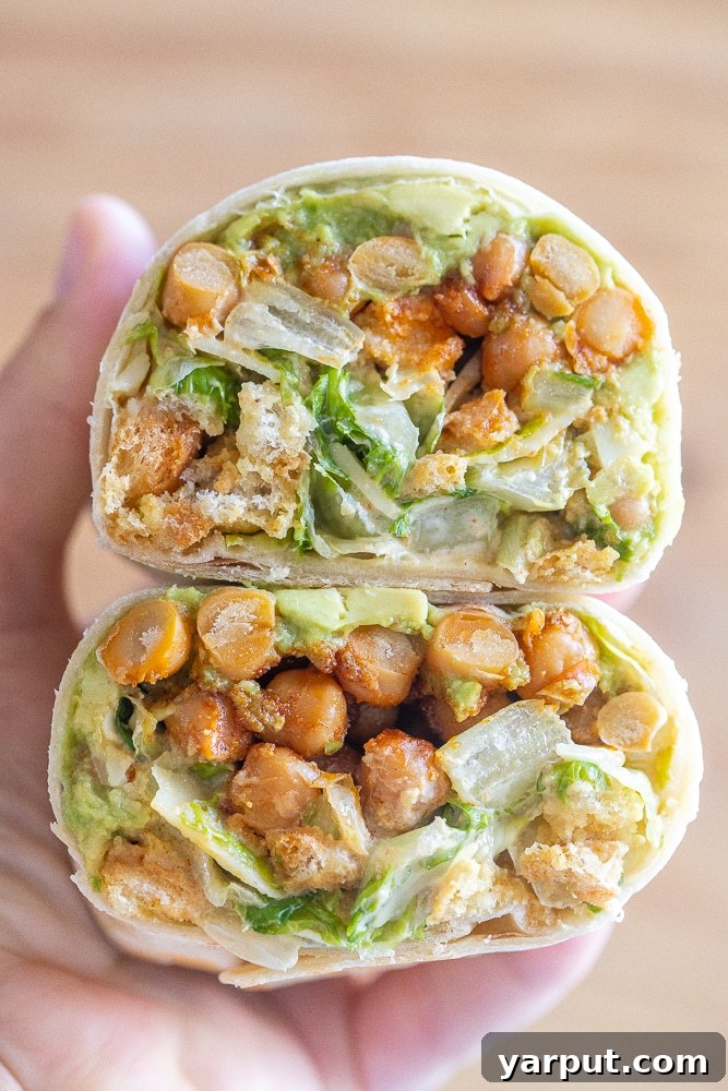 Two fresh and vibrant chickpea Caesar salad wraps, filled with crisp lettuce, creamy dressing, and seasoned chickpeas, served on a cutting board.
