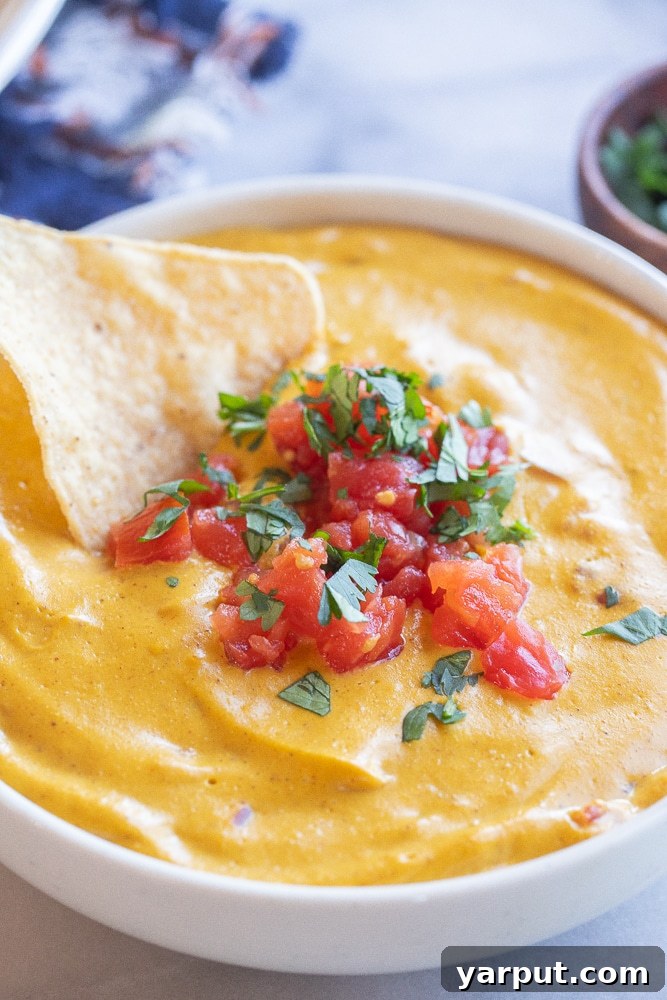 Creamy Plant Based Pumpkin Queso 7 close up shot of a tortilla chip being dipped into a bowl of creamy vegan cheese sauce, ready to be enjoyed