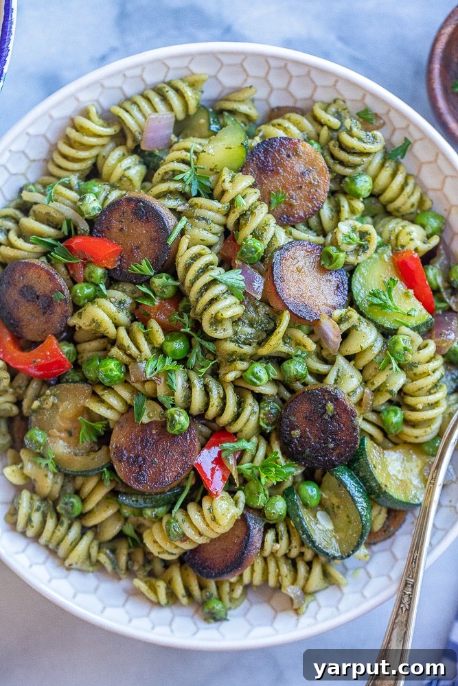 A close-up shot of Crispy Sausage Pesto Pasta served in a bowl, garnished with fresh herbs.