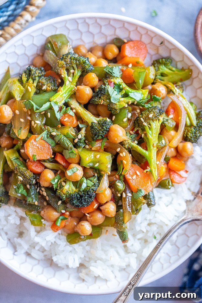 A close-up shot of a vibrant chili garlic vegetable stir fry with chickpeas served in a bowl, garnished with fresh herbs.