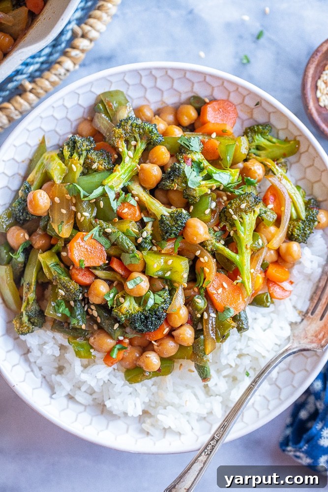 A beautifully set table featuring a bowl of garlic chili vegetables with chickpeas, accompanied by chopsticks and a glass of water, ready for a meal.