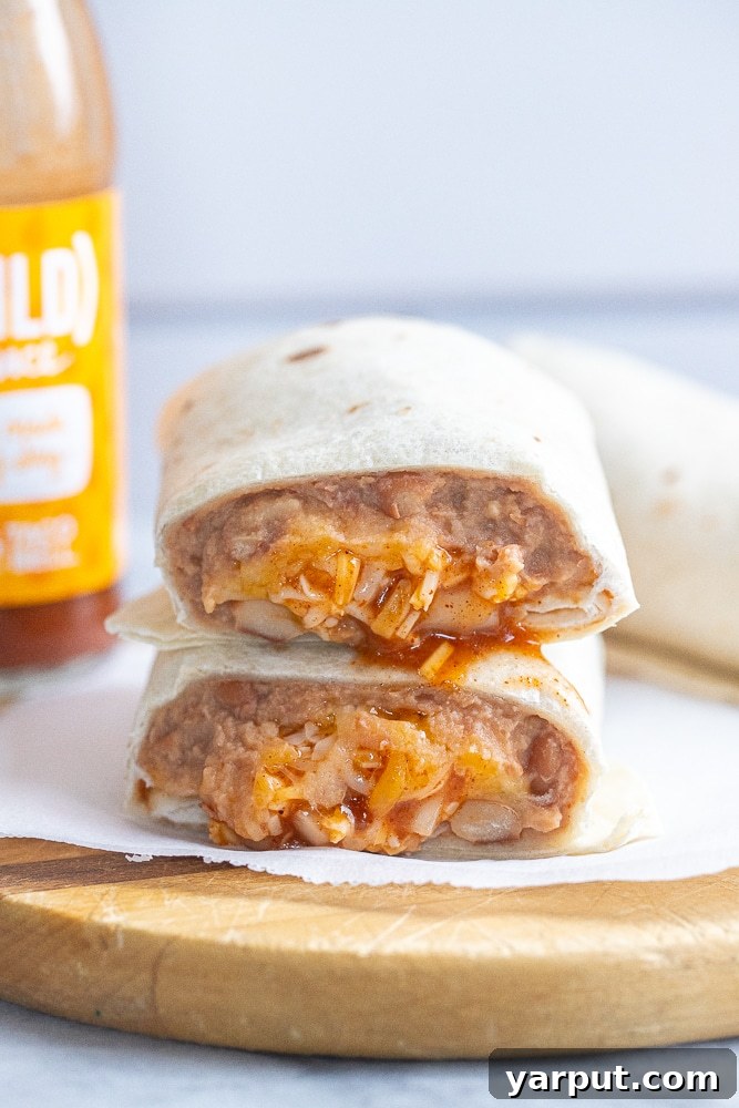 Homemade Taco Bell Bean Burrito Perfection 6 A Taco Bell copycat bean and cheese burrito recipe on a cutting board, perfectly sliced in half to reveal its delicious layers