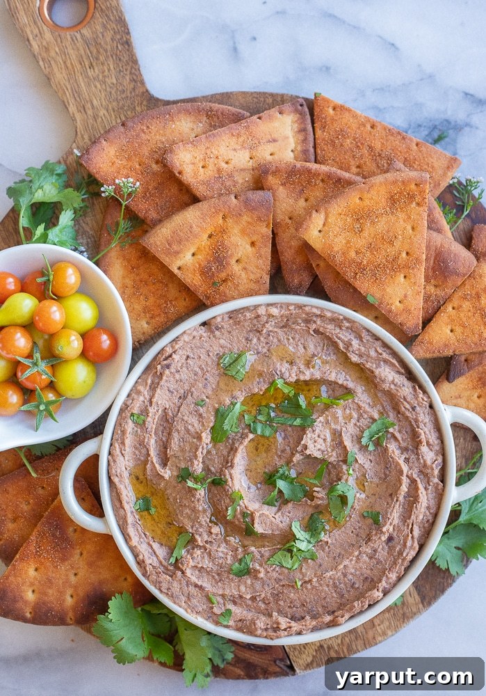 Smoky Black Bean Dip and Crispy Spiced Pita 7 A beautiful platter featuring a bowl of black bean hummus, surrounded by crispy pita chips and vibrant cherry tomatoes, creating an inviting appetizer spread.
