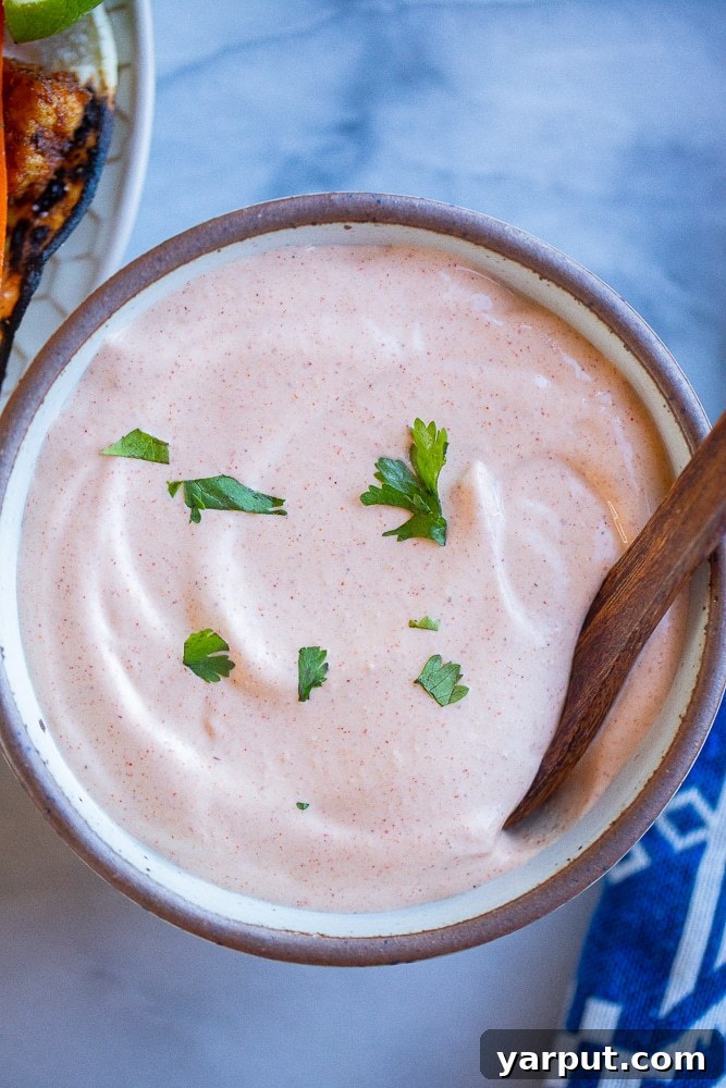 Creamy Zesty Fish Taco Sauce 5 Close-up of a serving bowl filled with creamy, light orange sour cream sauce, featuring a spoon scooping a portion.