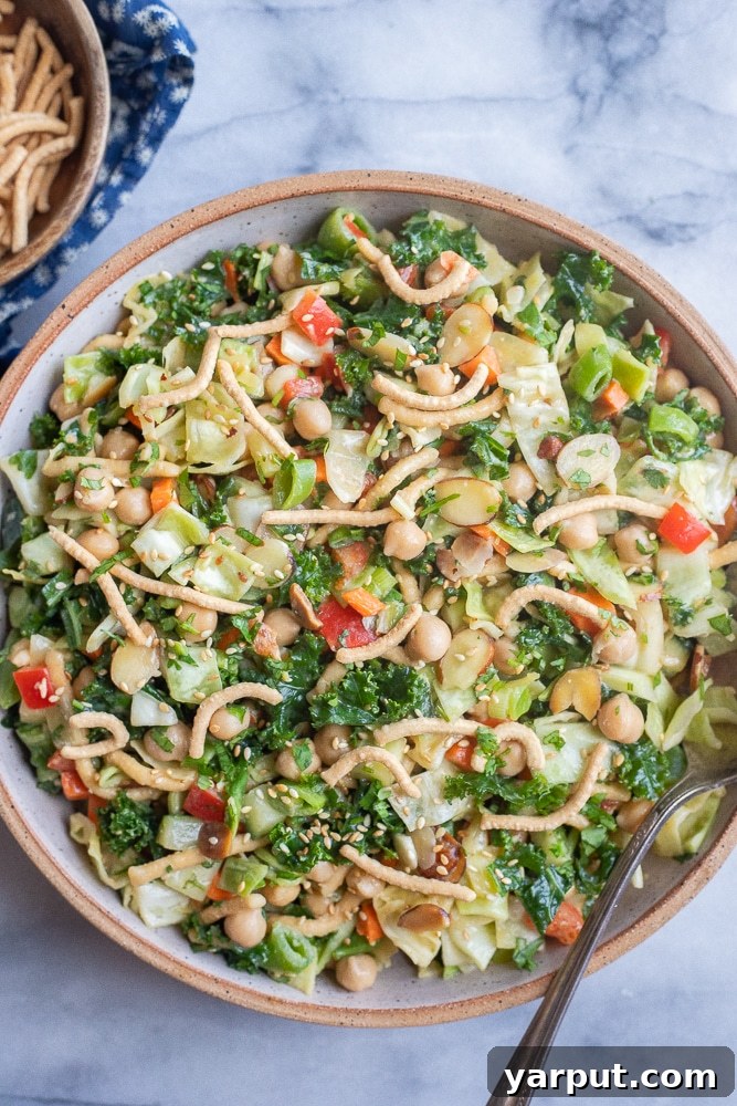 A large bowl of crunchy Chinese cabbage salad with chow mien noodles and chickpeas, garnished with sesame seeds.
