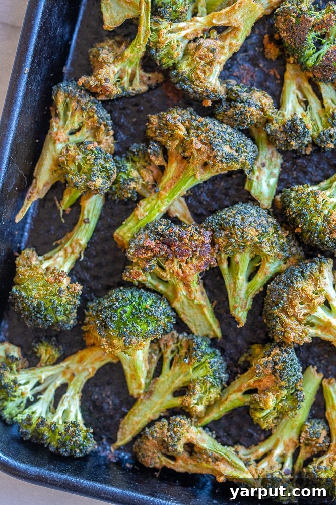 Close-up of a large baking sheet filled with an abundant amount of perfectly roasted broccoli, showing off its crispy, charred edges and golden-brown tahini coating.
