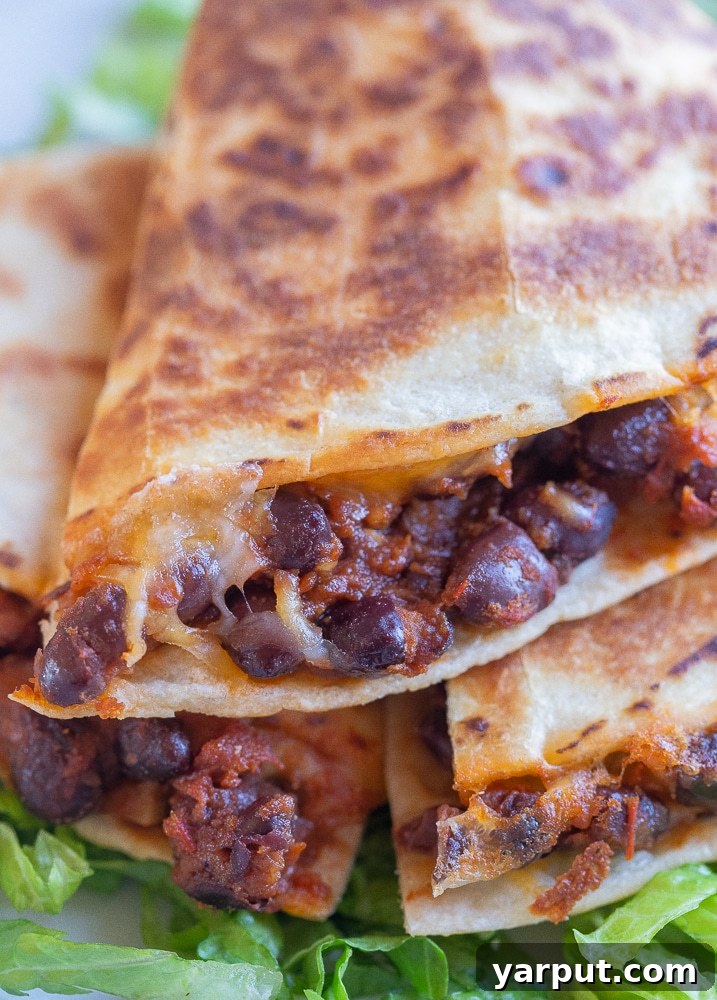 A close-up photograph of a BBQ Black Bean Quesadilla cut in half, revealing the cheesy, bean-filled interior and crispy tortilla texture.