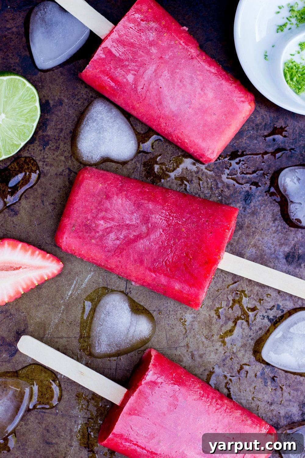 Tangy Strawberry Rhubarb and Lime Pops 2 Refreshing Strawberry Rhubarb & Lime Popsicles on a rustic sheet pan with ice cubes, ready to be enjoyed on a hot day