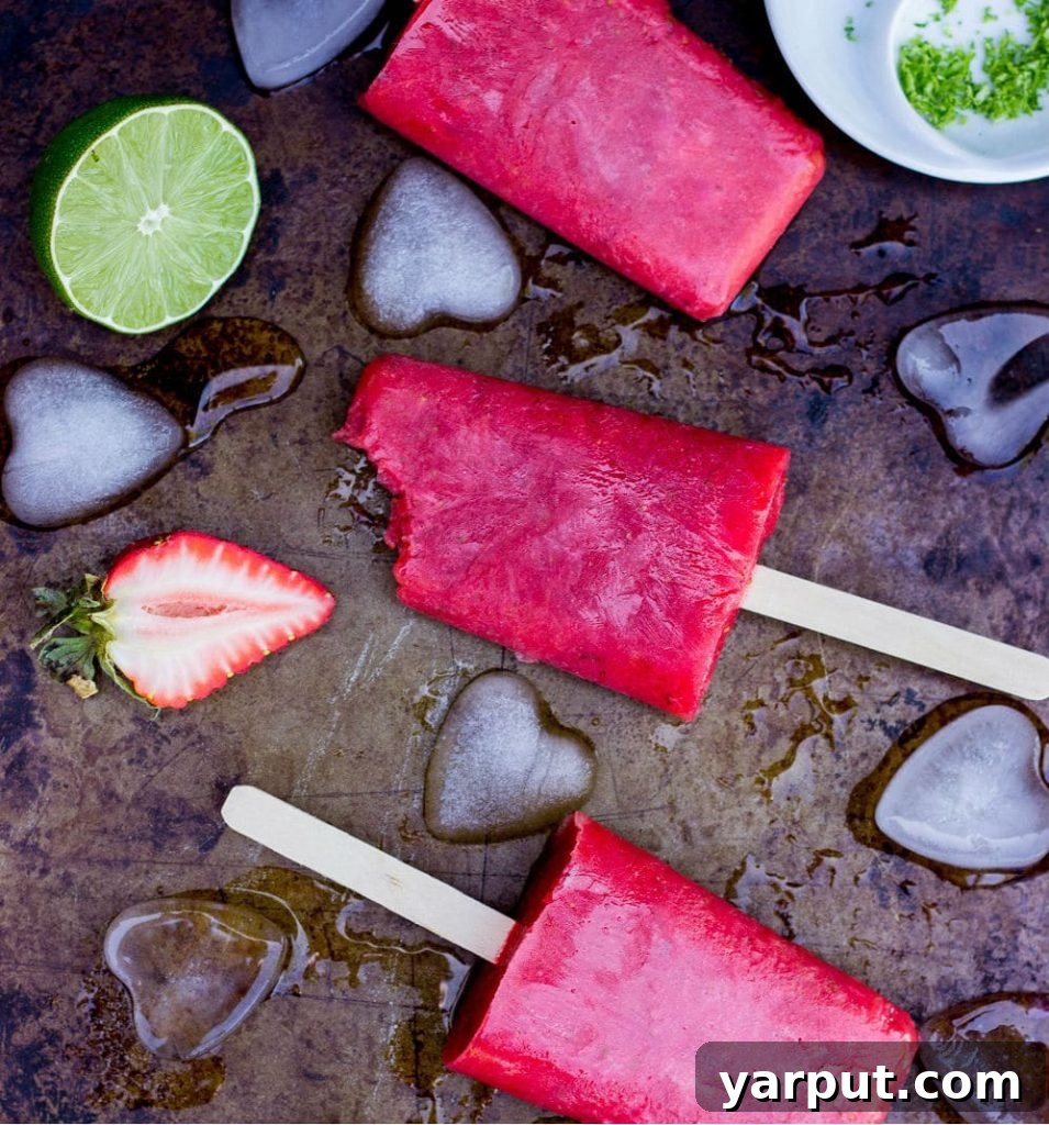 Tangy Strawberry Rhubarb and Lime Pops 10 Close-up of a Strawberry Rhubarb & Lime Popsicle being unwrapped, showing its icy texture and the visible fruit pieces