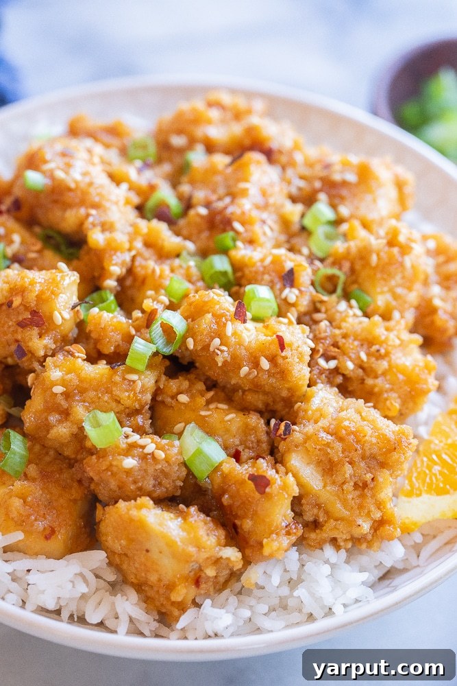 Crispy, golden-brown tofu coated in a glossy, spicy orange ginger sauce, garnished with sesame seeds and green onions.