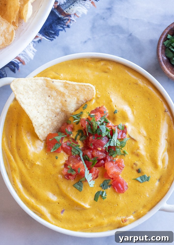 The Ultimate Vegan Thanksgiving Menu and Shopping List 3 A vibrant bowl of Vegan Pumpkin Queso Dip, rich and orange-hued, served with a pile of crispy tortilla chips on the side. The dip looks smooth and inviting, perfect for scooping.