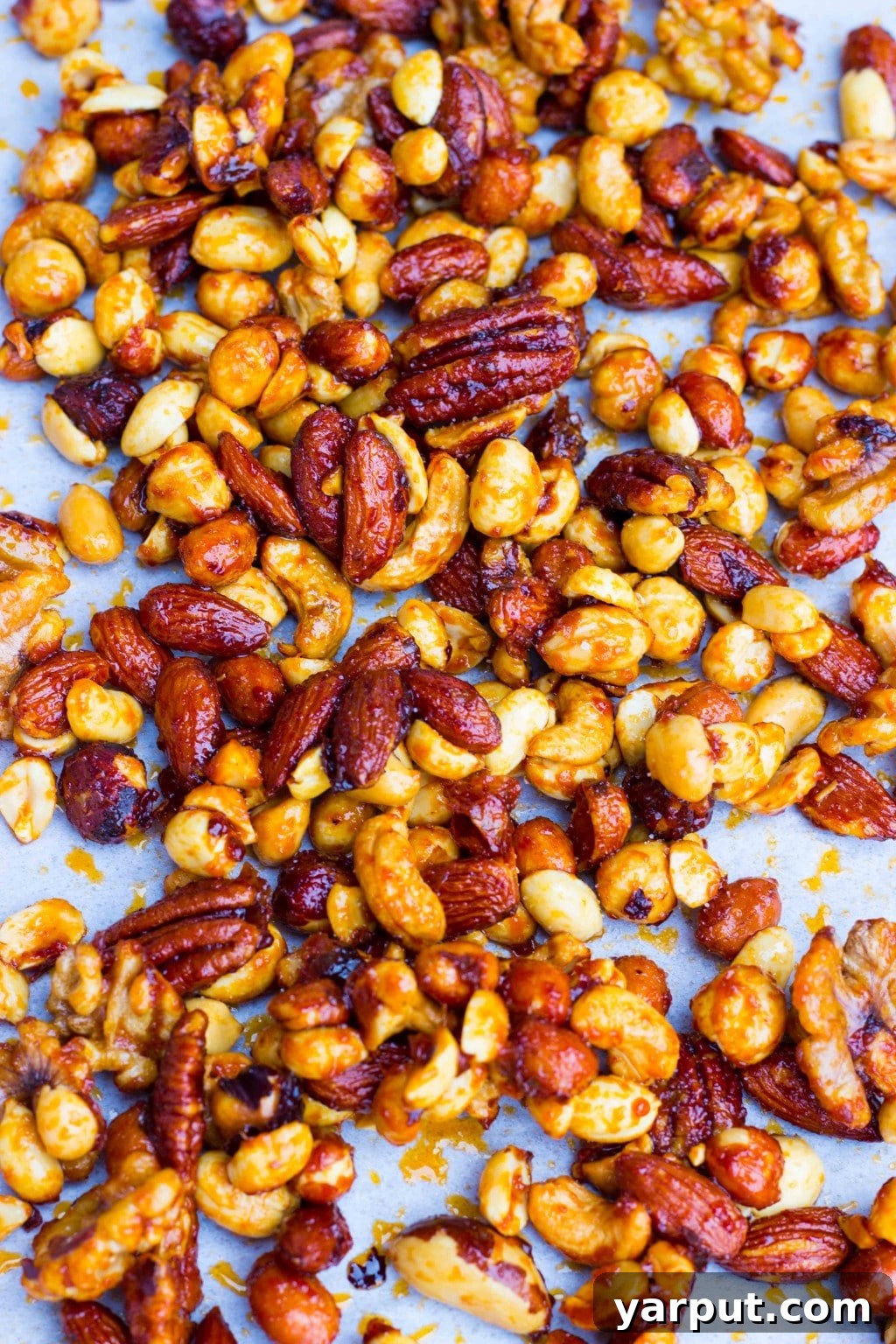 The Ultimate Vegan Thanksgiving Menu and Shopping List 4 A close-up shot of Sriracha and Maple Roasted Mixed Nuts, glistening with a sweet and spicy glaze. Various nuts are visible, suggesting a rich texture and complex flavor profile, ready for snacking.