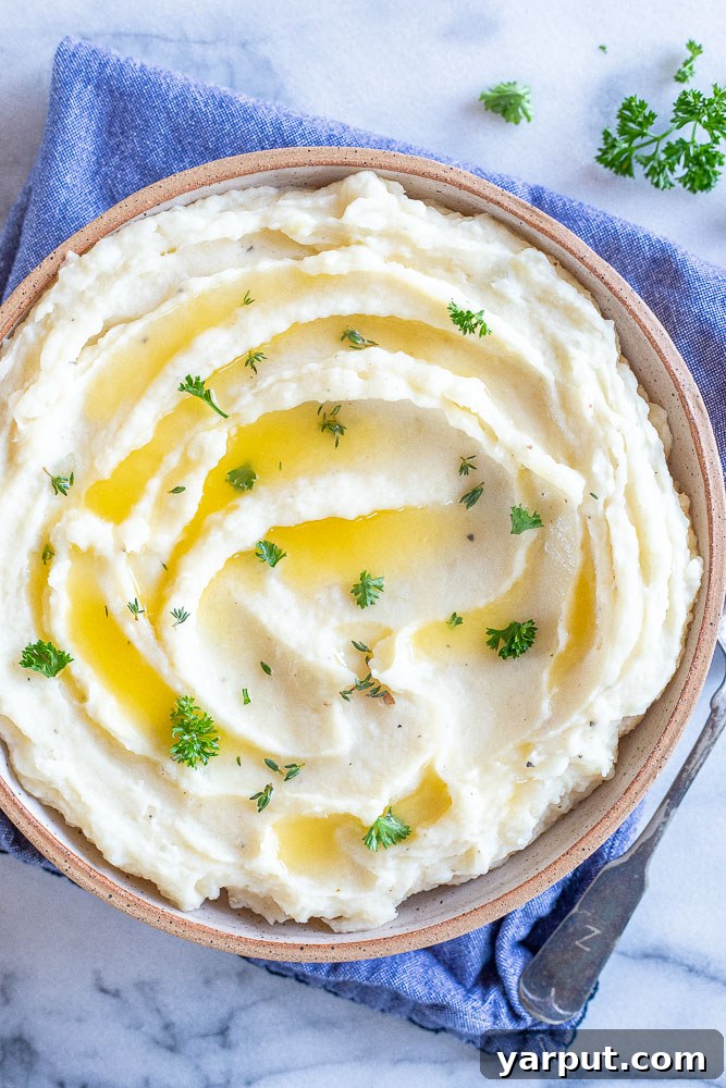 The Ultimate Vegan Thanksgiving Menu and Shopping List 9 A bowl of incredibly creamy Vegan Mashed Potatoes, garnished with fresh herbs, suggesting a rich and comforting texture. A pat of vegan butter is melting on top, adding to the visual appeal.