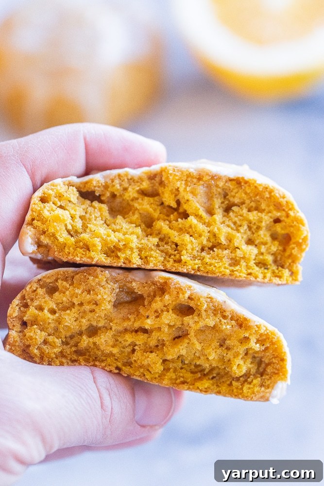 Pillowy Pumpkin Cookies with Zesty Orange Glaze 7 a hand holding a pumpkin cookie that has been broken in half, revealing its moist interior