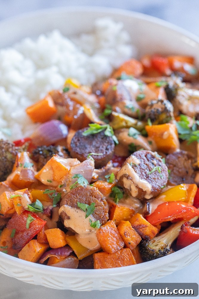 BBQ Tahini Roasted Veggie Sheet Pan Bliss 5 A close-up view of a vibrant vegan sheet pan dinner served over rice, richly drizzled with a creamy tahini dressing and garnished with fresh herbs, showcasing the perfectly roasted vegetables and plant-based sausage.