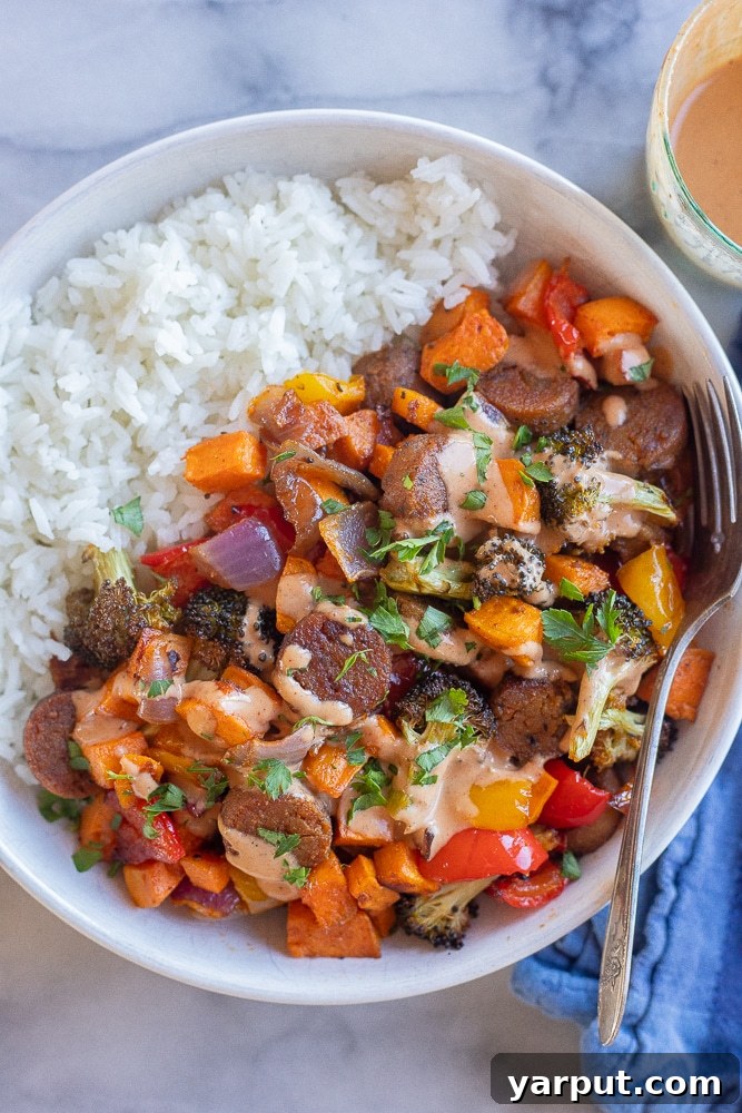 BBQ Tahini Roasted Veggie Sheet Pan Bliss 7 A close-up of a cozy dinner bowl showcasing the easy vegetarian sheet pan dinner with plant-based sausage, roasted vegetables, served over rice and generously drizzled with BBQ tahini sauce, ready to be enjoyed.