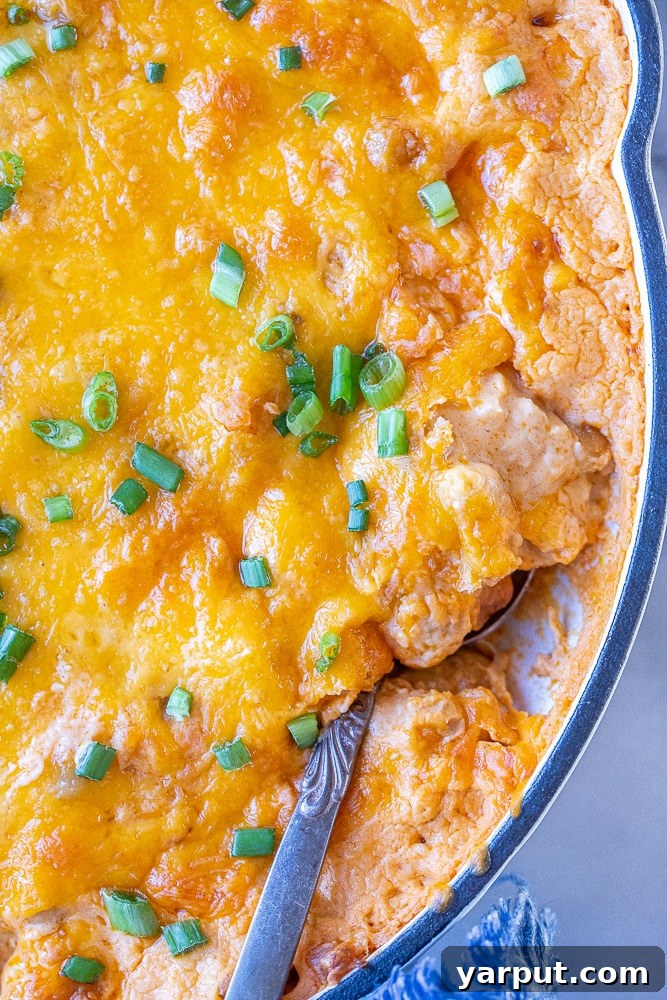 Ultimate Plant-Based Buffalo Chickpea Dip 6 A close-up shot of a spoonful of creamy buffalo chickpea dip in a hot skillet, ready to be served.