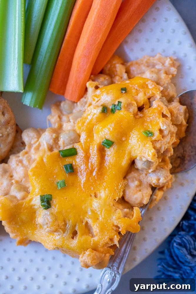 Ultimate Plant-Based Buffalo Chickpea Dip 7 A close-up of a generous scoop of buffalo chickpea dip on a plate, garnished with fresh carrots and celery sticks.