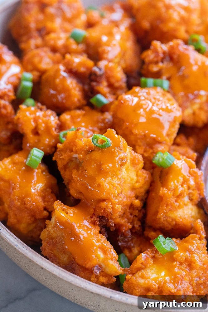 Irresistible Vegan Buffalo Tofu Wings 5 A close-up photograph of a heaping bowl of freshly baked vegan buffalo tofu wings, garnished with chopped green onions, ready to be served as a delicious appetizer.