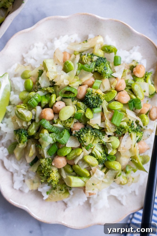 Emerald Veggie & Chickpea Skillet 2 A vibrant bowl of green vegetable stir fry featuring broccoli, cabbage, edamame, and chickpeas, served over fluffy white rice. Garnished with fresh herbs and a lime wedge, ready to be enjoyed as a healthy, easy spring meal.