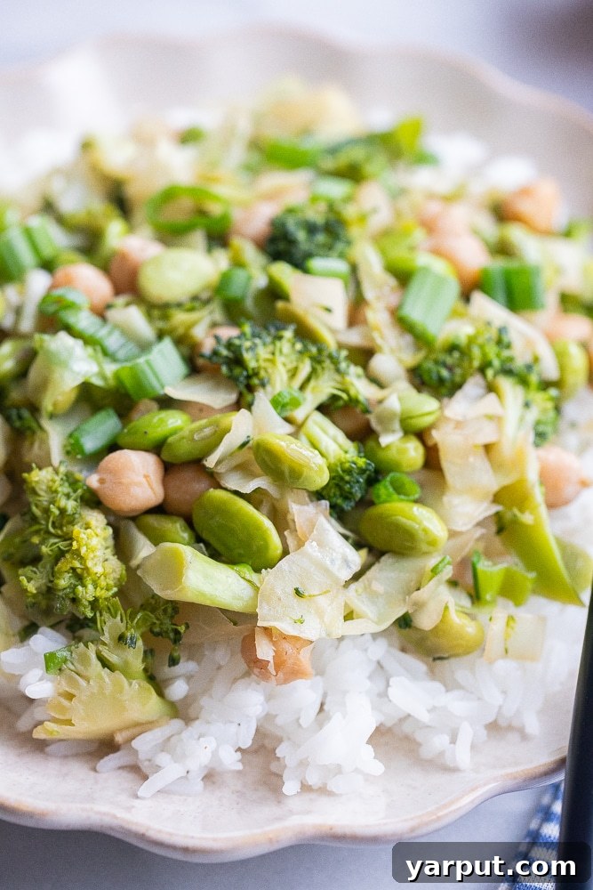 Emerald Veggie & Chickpea Skillet 6 A close-up view of a healthy and vibrant green vegetable stir fry, showcasing tender broccoli florets and shelled edamame glistening with a savory sauce, served over a bed of fluffy white rice.