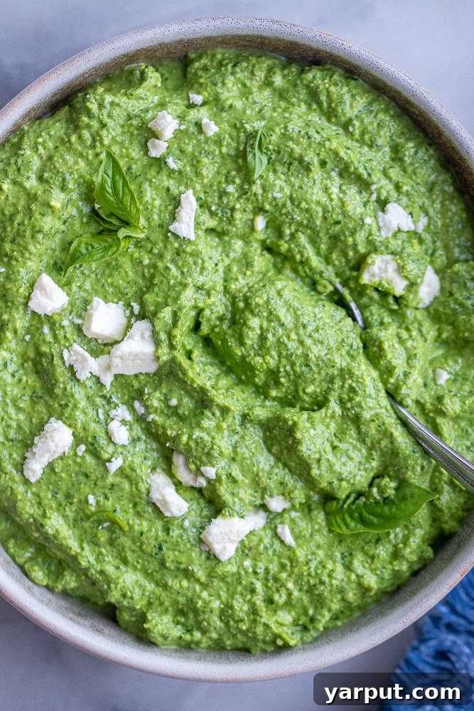 Mediterranean Feta & Spinach Pesto 2 A beautiful bowl of creamy feta pesto sauce, garnished with fresh basil leaves and crumbled feta, with a spoon ready for serving.