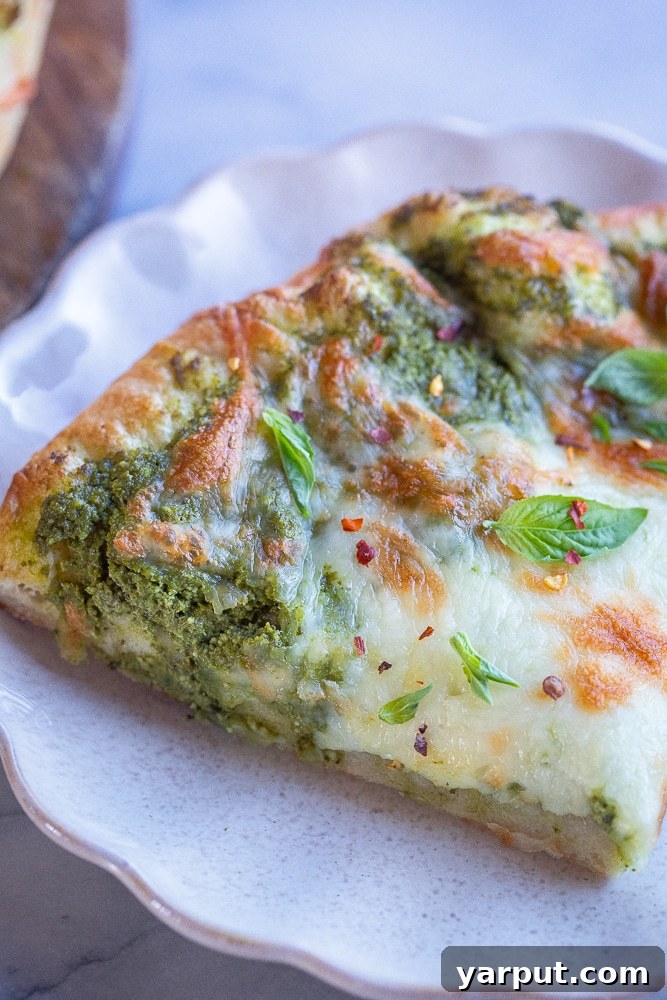 Ultimate Pesto Pizza Delight 6 A close-up shot of a single slice of the best vegetarian pesto pizza on a white plate, showcasing its creamy pesto base, melted mozzarella, and fresh basil garnish
