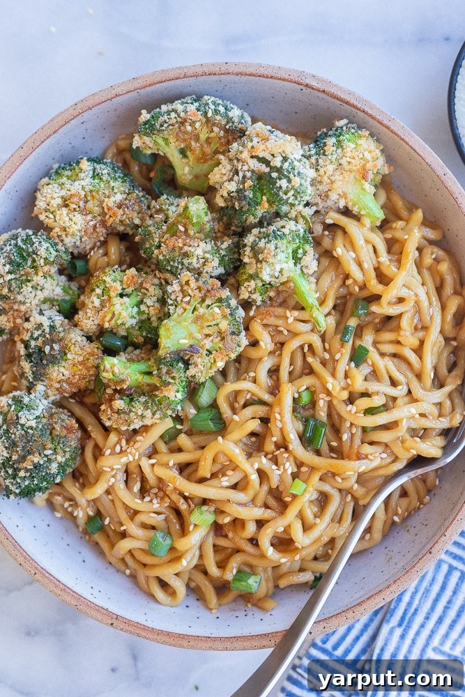 Sticky Teriyaki Noodles with Crispy Roasted Broccoli 2 A vibrant bowl of saucy teriyaki noodles topped with perfectly golden-brown crispy baked broccoli florets, garnished with fresh green onions.