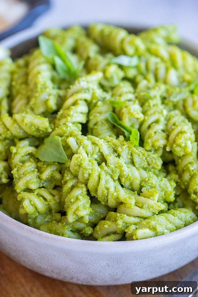 A tantalizing close-up shot of a bowl filled with Green Goddess Pesto Pasta, showcasing the rich, vibrant green sauce clinging to every noodle, inviting you to take a bite.