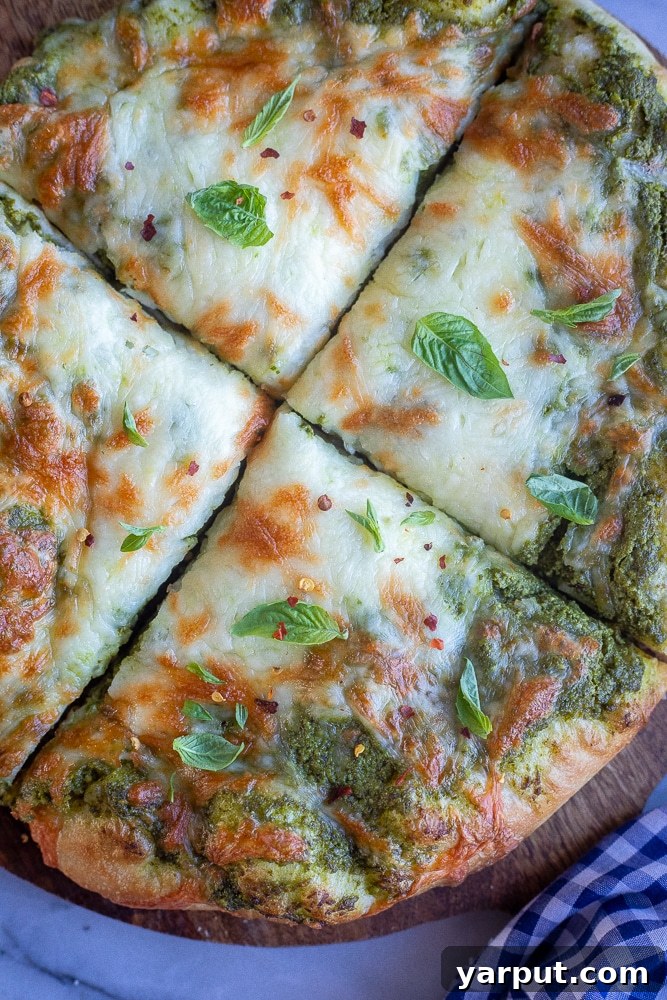 Effortless Meatless Meals: Week 5 Menu 7 A freshly baked pesto pizza, topped with cheese and fresh basil leaves, ready to be sliced.