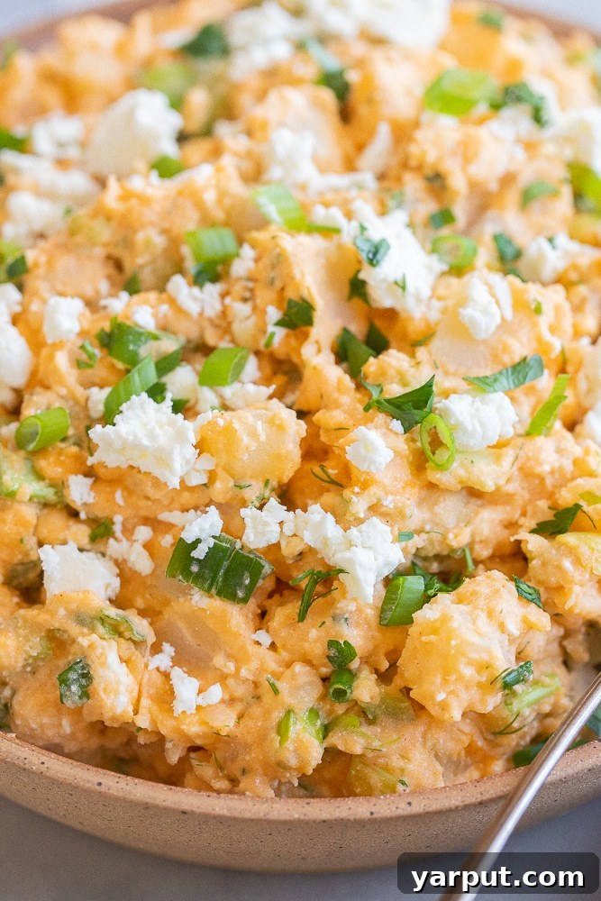 close up of a bowl of buffalo potato salad, garnished with fresh herbs and feta