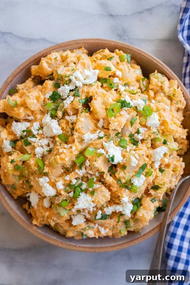 bowl of buffalo potato salad topped with feta cheese and green onion and herbs