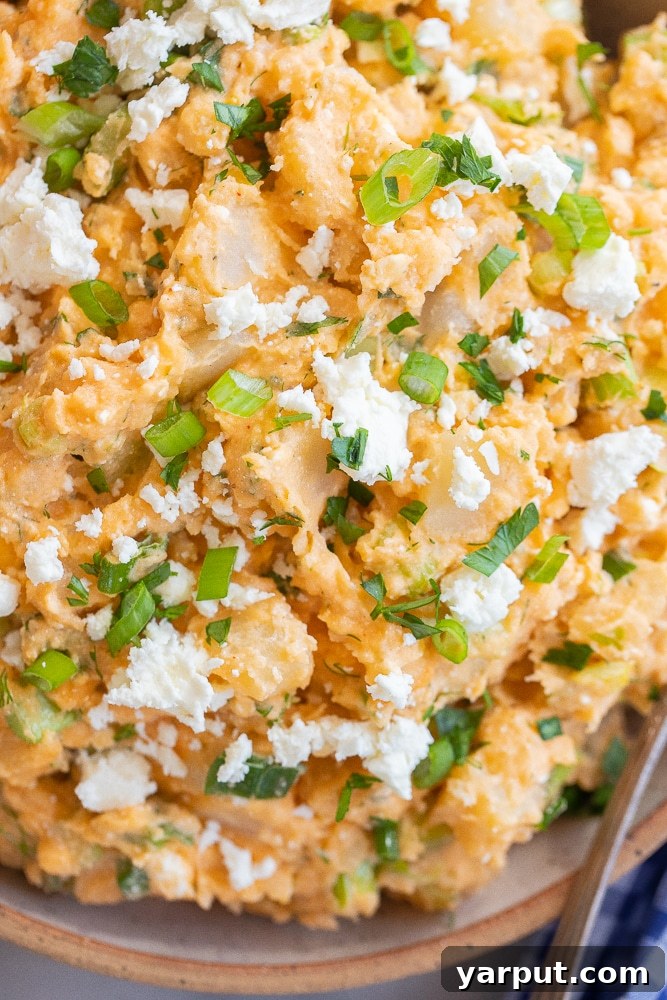 close up of bufalo flavored potato salad in a white bowl with green onions