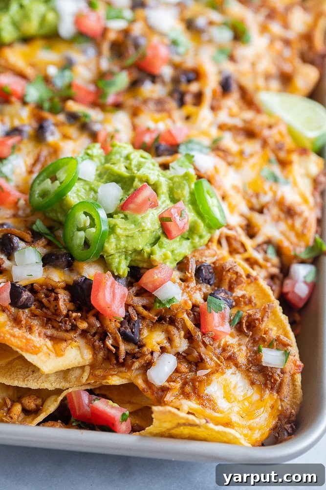Zesty Tofu Crumble Nacho Platter 6 Close-up view of a pan of ultimate shredded tofu nachos, beautifully topped with fresh guacamole