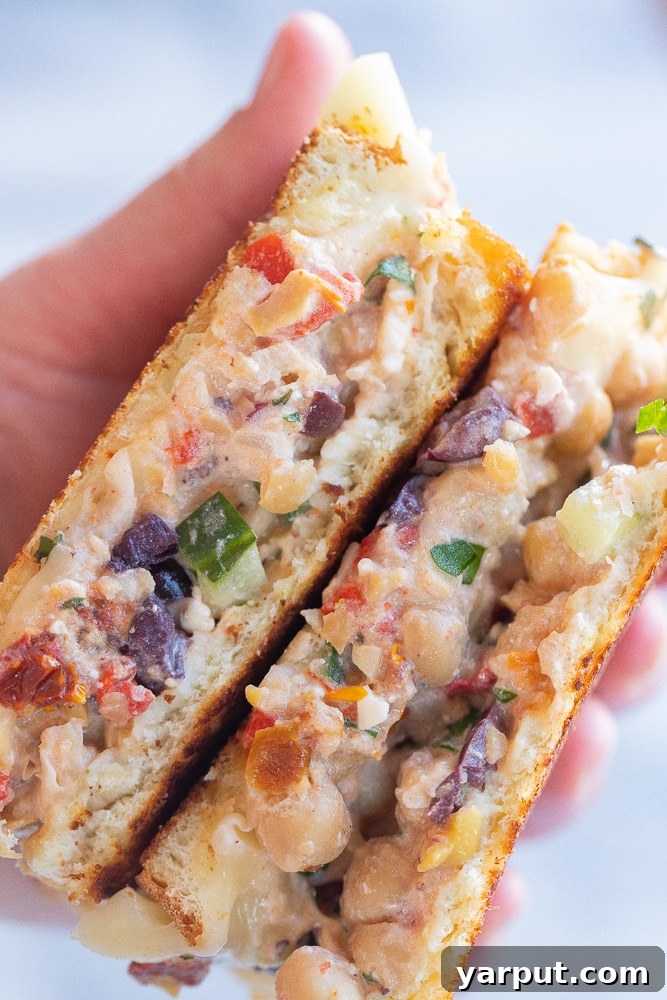 Grecian Chickpea Toasties 5 A hand holding a sliced open Greek chickpea salad melt, showing the vibrant filling and melted cheese.