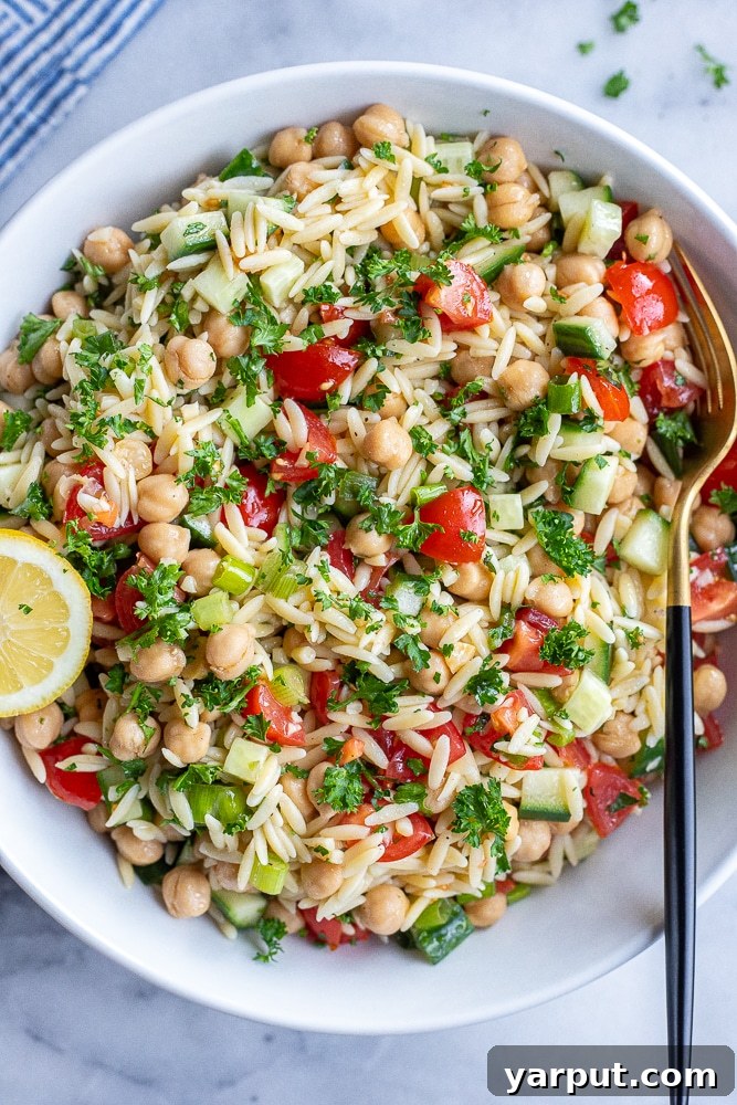 Vibrant Mediterranean Orzo & Chickpea Salad 2 A vibrant serving bowl filled with Tabouli Inspired Orzo Salad, featuring chickpeas, fresh herbs, tomatoes, and cucumber, garnished with a lemon wedge.