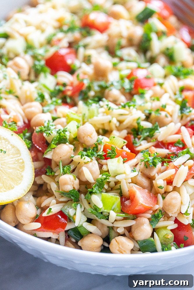 Vibrant Mediterranean Orzo & Chickpea Salad 6 A beautiful large serving bowl of Tabouli Inspired Orzo Salad with chickpeas, garnished with a fresh lemon wedge, ready to be enjoyed.