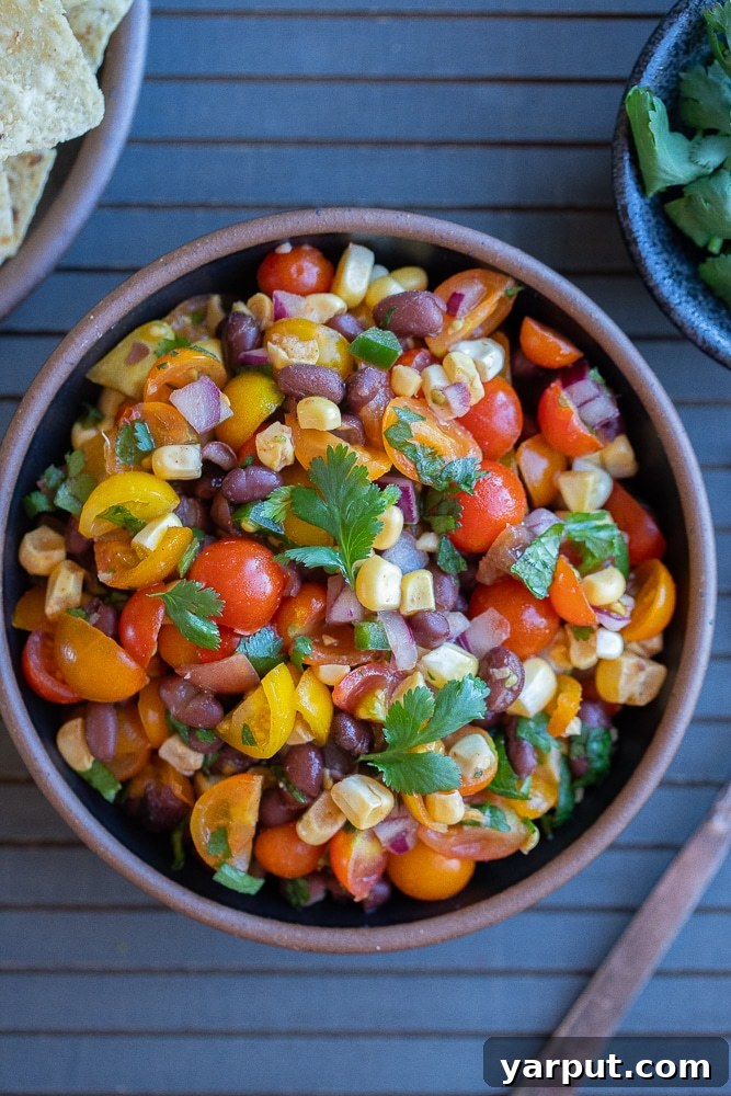 A beautiful serving bowl brimming with homemade black bean and corn salsa, featuring vibrant cherry tomatoes and fresh herbs, ready for a gathering.