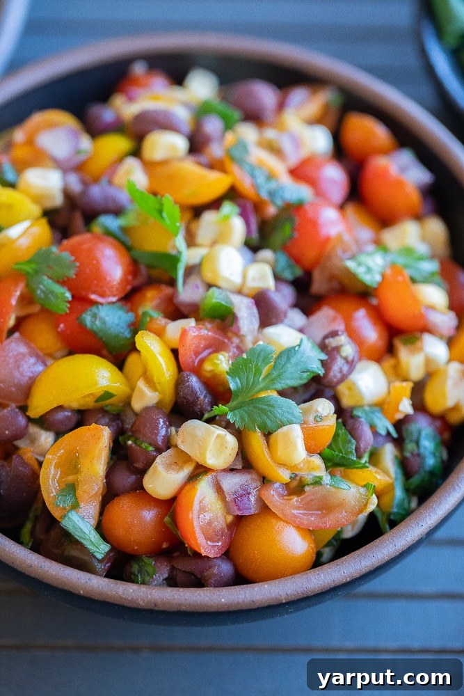 Close-up shot of homemade cherry tomato, black bean, and corn salsa, garnished with fresh cilantro, highlighting its chunky texture and vibrant colors.