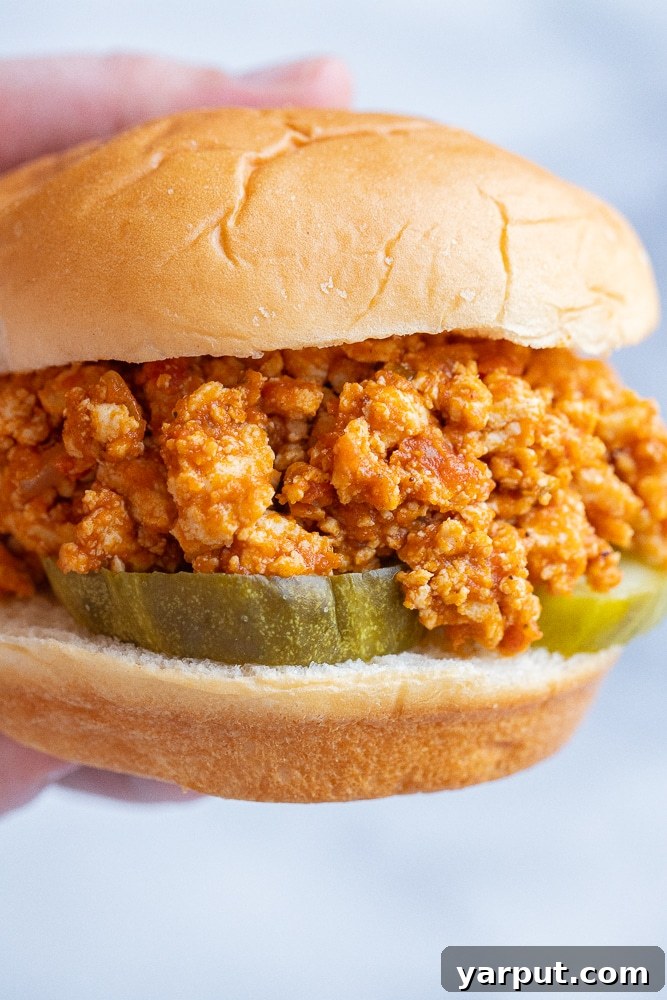close up of a hand holding a pumpkin sloppy joe with pickles