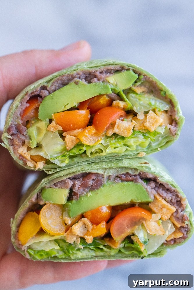 Crispy Black Bean Ranch Pinwheels 2 Close up of a crunchy black bean ranch wrap cut in half, held by a hand, showing off its vibrant layers of ingredients.